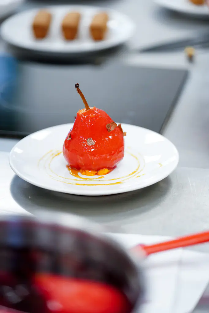poire pochée glacée au sucre caramélisé dressée sur une assiette en cuisine