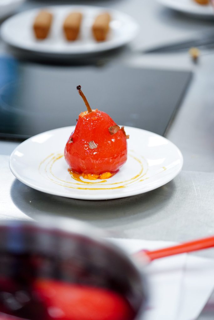 poire pochée glacée au sucre caramélisé dressée sur une assiette en cuisine