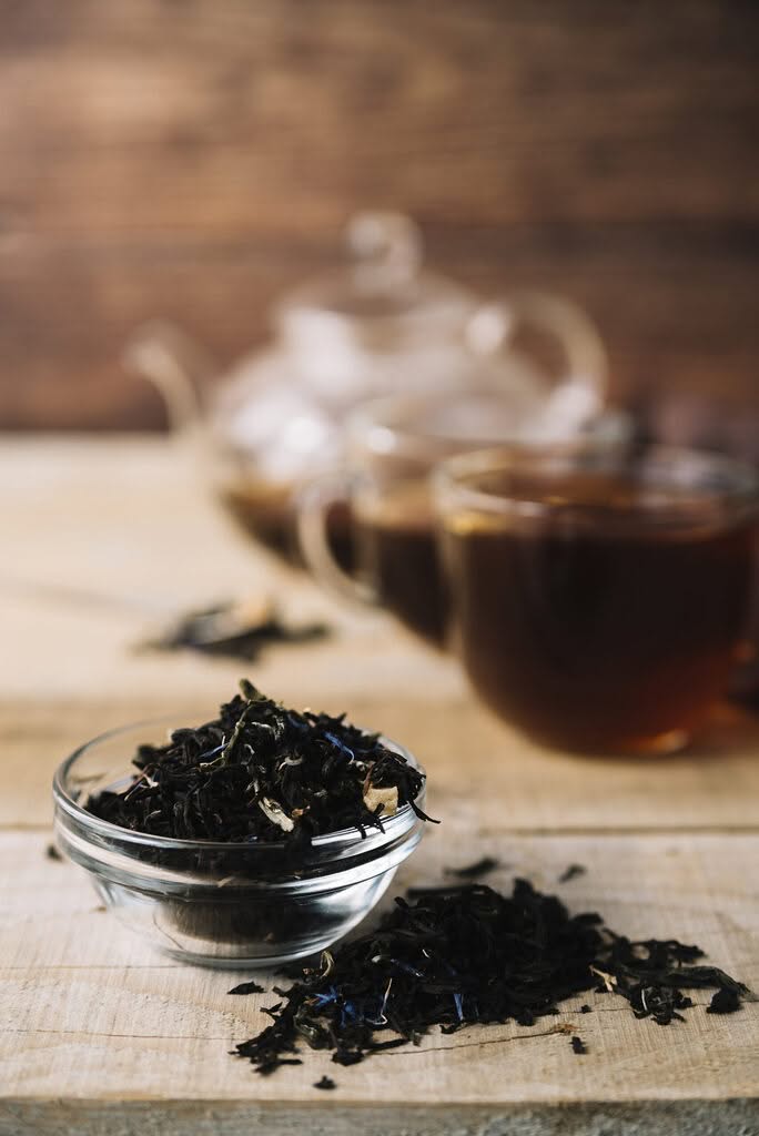 feuilles de thé noir en vrac dans un bol avec infusion de thé en arrière-plan