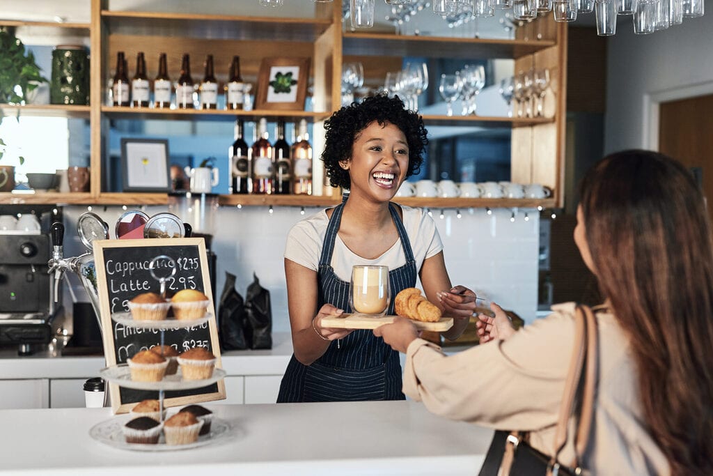 serveuse souriante servant un client dans un coffee shop illustrant une expérience inclusive et une offre adaptée à tous les profils